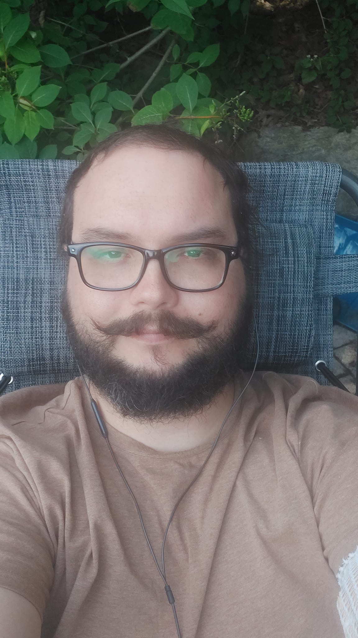 A man short hair and bushy facial hair reclines on a folding chair